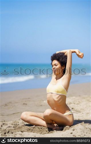 Black woman, wearing a yellow bikini, sitting on the beach relaxing and stretching her body.. Black girl, wearing a yellow bikini, sitting on the beach relaxing and stretching her body.