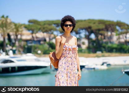 Black woman with afro hairstyle in summer dress, walking through a harbour full of boats. Girl enjoying her holiday in a coastal area.. Black woman with afro hairstyle in summer dress, walking through a harbour full of boats.
