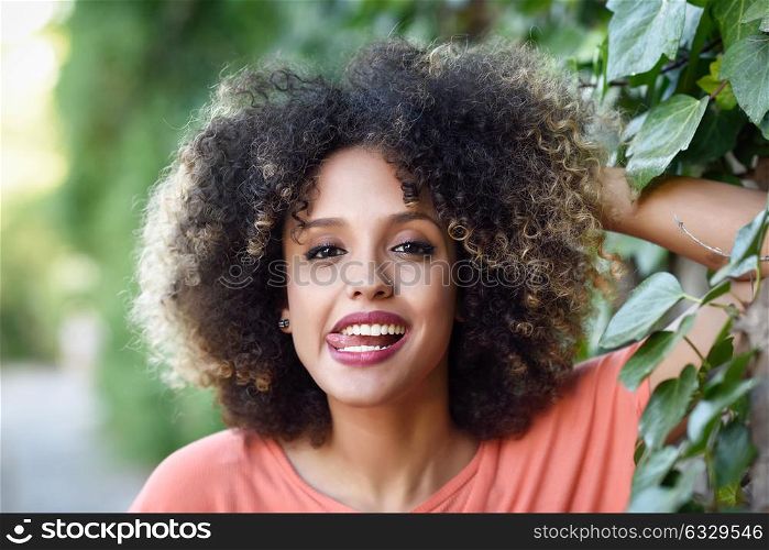 Black woman with tongue out in an urban park. Young mixed girl with afro hairstyle. Funny female.