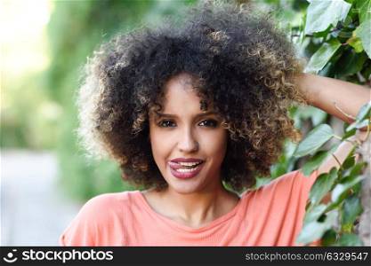 Black woman with tongue out in an urban park. Young mixed girl with afro hairstyle. Funny female.