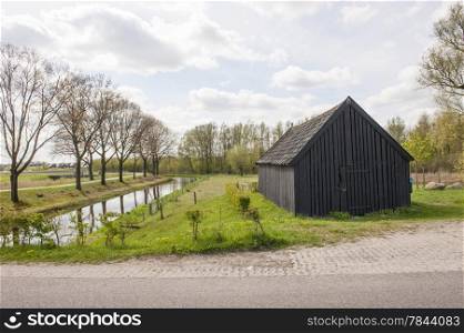 Black wooden barn near canal in rural scenery