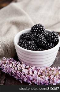 Blackberry in white bowl and flowers on wooden background. Natural healthy food.Still life photography