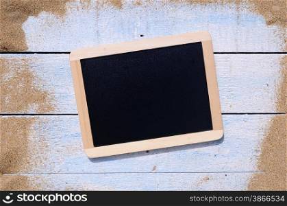 Blackboard and blue wooden table on beach sand.