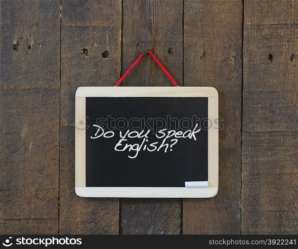 Blackboard hanging on a old wooden wall with phrase do you speak english.