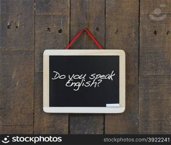 Blackboard hanging on a old wooden wall with phrase do you speak english.