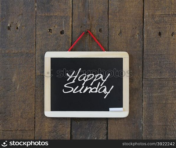 Blackboard hanging on a old wooden wall with phrase Happy Sunday.