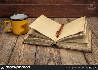 blank antique≤ather-bound journal with decked ed≥handmade paper pa≥s with a stylish pen and cup of tea on rustic wood, journaling concept