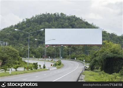 Blank billboard sign by empty highway through forest mountains landscape