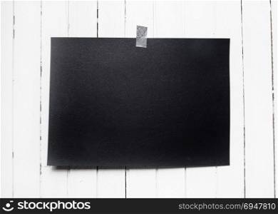 Blank black poster hanging on a tape on white wooden plank wall. Template background for your design.. Blank black poster hanging on a tape on white wooden plank wall.