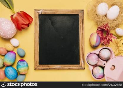 blank blackboard with fresh flowers decorated easter eggs yellow backdrop