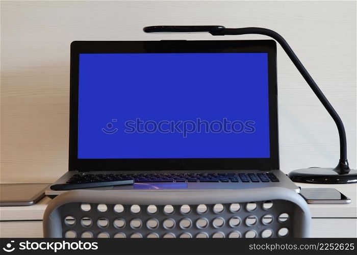 blank blue screen laptop computer with table lamp is on twooden desk as workplace concept