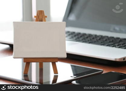 blank canvas and wooden easel on laptop computer as concept