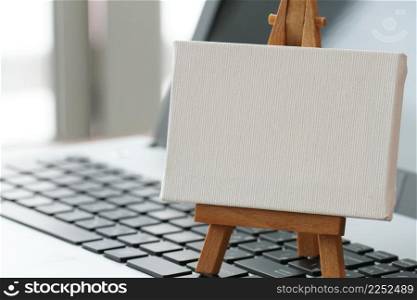blank canvas and wooden easel on laptop computer as concept