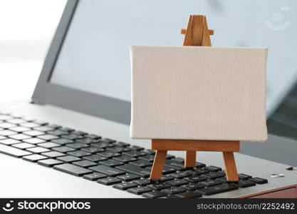 blank canvas and wooden easel on laptop computer as concept