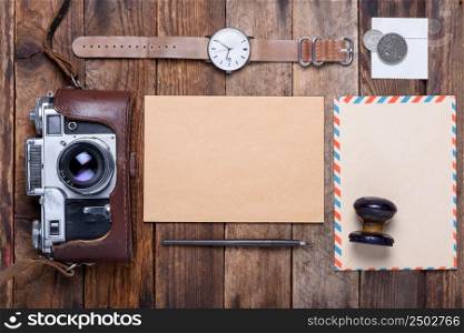 Blank card with envelope and vintage camera, stamps, watch, ink pen on wooden table still life