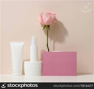 blank cardboard business card and a set of jars, tubes and plastic bottles on a beige background. Cosmetic branding, promotion and advertising