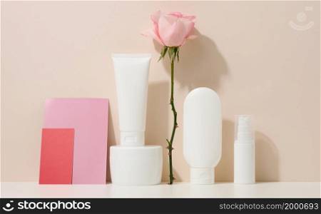 blank cardboard business card and a set of jars, tubes and plastic bottles on a beige background. Cosmetic branding, promotion and advertising