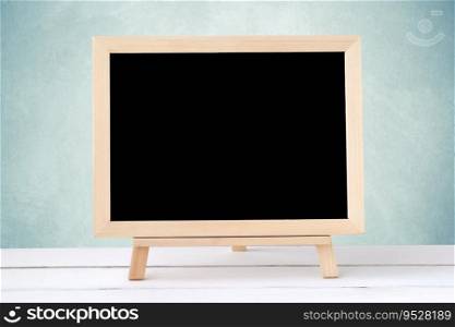 Blank chalkboard standing on white table over green cement wall background, space for text