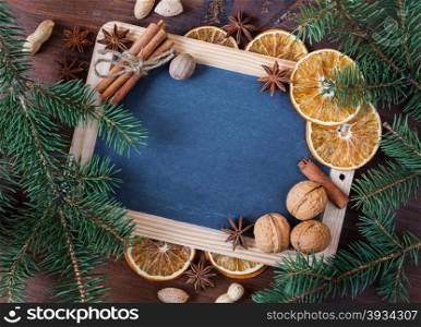 Blank chalkboard surrounded by green fir branches, different spices and dried oranges