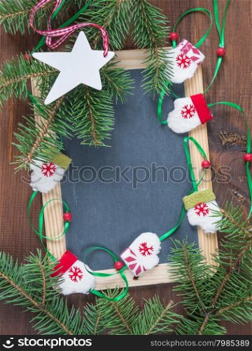 Blank chalkboard surrounded by green fir branches, doll mittens and white wooden star