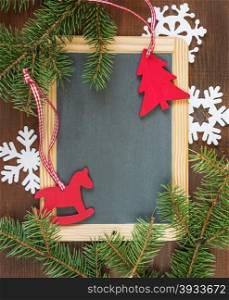 Blank chalkboard surrounded by green fir branches, white felts snowflakes and red rocking horse and spruce