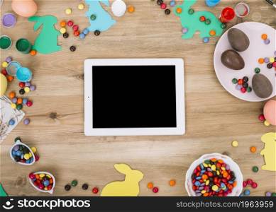 blank digital tablet surrounded with colorful gems candies easter eggs paper cutout bunny wooden table. High resolution photo. blank digital tablet surrounded with colorful gems candies easter eggs paper cutout bunny wooden table. High quality photo