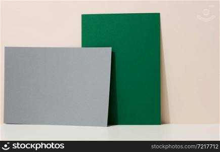 blank green and gray cardboard sheet of paper with shadow on white table. Template for flyer, announcement