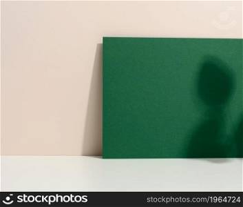 blank green cardboard sheet of paper with shadow on white table. Template for flyer, announcement