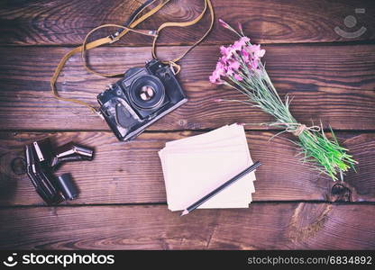 Blank greeting card and old vintage film camera on a brown wooden background, top view, vintage toning