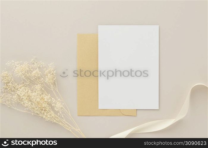 Blank greeting card invitation Mockup 5x7 on Brown envelope with dried flowers on beige background, flat lay, mockup
