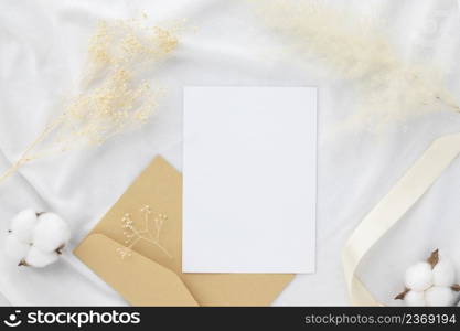 Blank greeting card invitation Mockup 5x7 on envelope with dry flowers and ribbon on white fabric background, flat lay, mockup 
