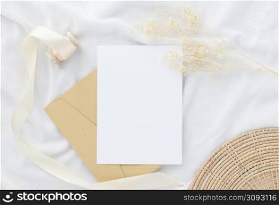 Blank greeting card invitation Mockup 5x7 on envelope with dry flowers and ribbon on white fabric background, flat lay, mockup