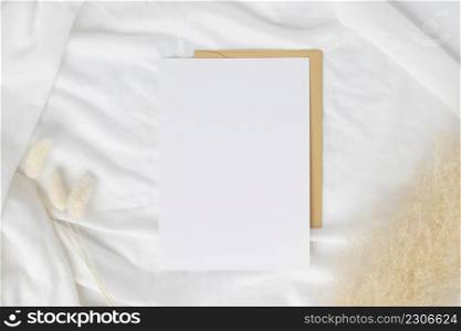 Blank greeting card invitation Mockup on Brown envelope with Dried bunny tails grass on white background, Minimal table workplace composition, flat lay, mockup