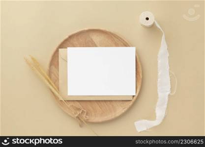Blank greeting card invitation Mockup on Brown envelope with Dried bunny tails grass on beige background, Minimal table workplace composition, flat lay, mockup