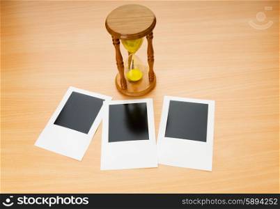 Blank instant photos and hour glass on the wooden table