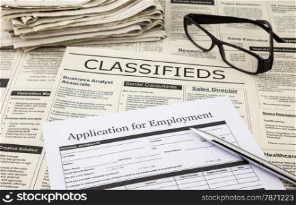 blank job application form place on fake classifieds ads with stack of newspaper and glasses