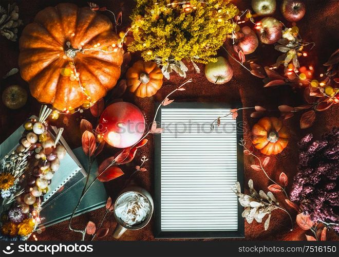 Blank letter board on dark background with cozy autumn home arrangement: leaves, pumpkins, fall flowers,burning candles,books, cup of hot chocolate or coffee. Top view. Blog layout. Flat lay