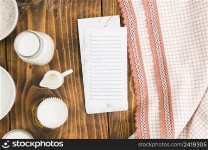 blank list notepad with milk jar cup cake mold wooden desk near table cloth