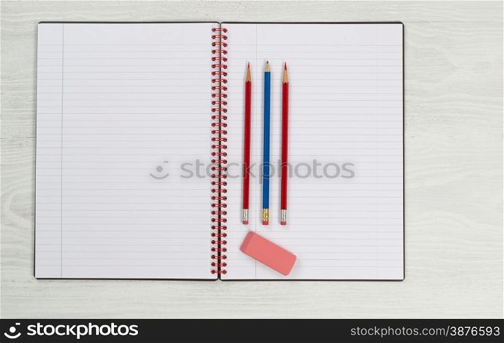 Blank new notepad, in open position, with sharpen pencils and eraser on rustic white desktop.