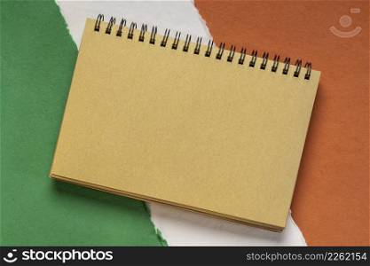 blank notebook against paper abstract in colors of national flag of Ireland (green, white and orange)