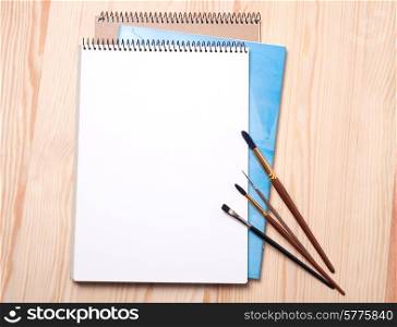 Blank notebook and brushes on a wooden background