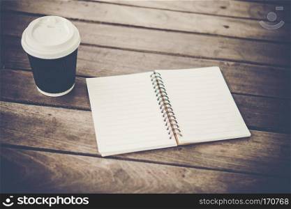 Blank notebook and cup of coffee on a wooden table.