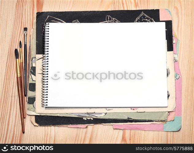 Blank notebook, brushes and old paper sheet on a wooden surface