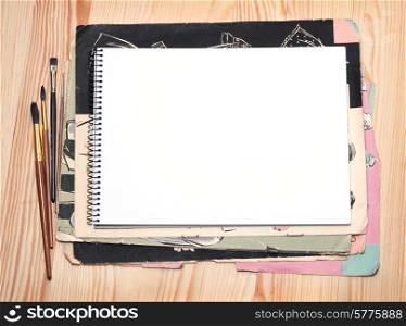 Blank notebook, brushes and old paper sheet on a wooden surface