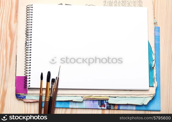 Blank notebook, brushes and old paper sheet on a wooden surface