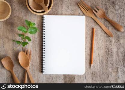 Blank notebook for text note on wooden table background. On wooden have spoon fork and pencil
