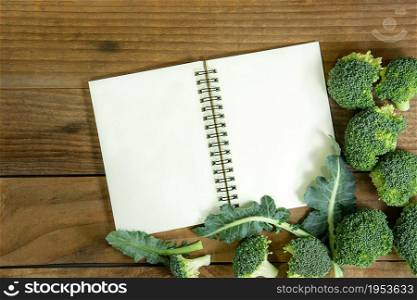 blank notebook with fresh broccoli on wooden table