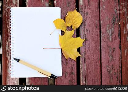 Blank notepad and pencil on the wooden background with autumn leaf