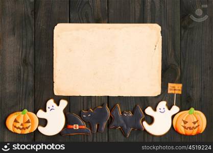 Blank old paper sheet and gingerbread cookie over dark wooden background. Halloween invitation.