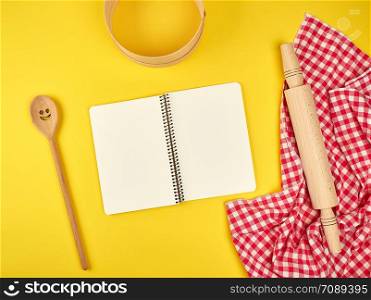 blank open notebook and wooden kitchen accessories, round sieve, rolling pin , recipe concept, yellow background